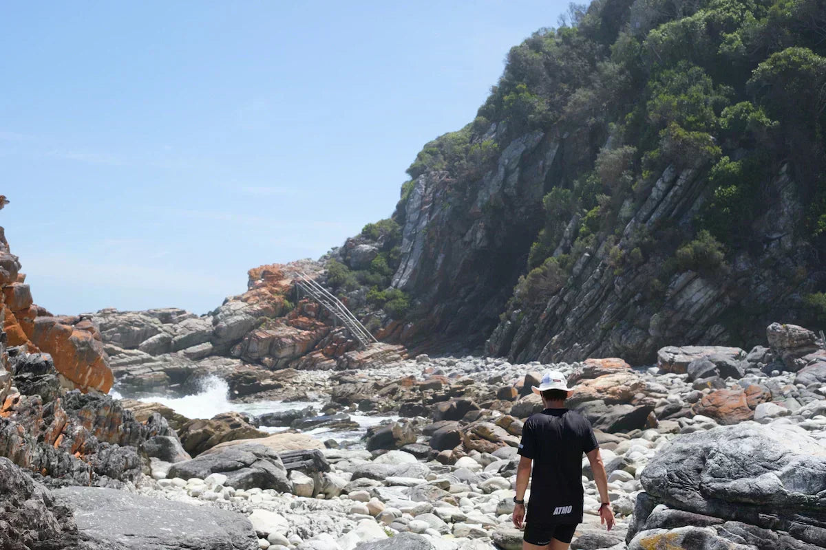 Runner walking along a rocky coastal path with cliffs and ocean in the background in Storms River, South Africa