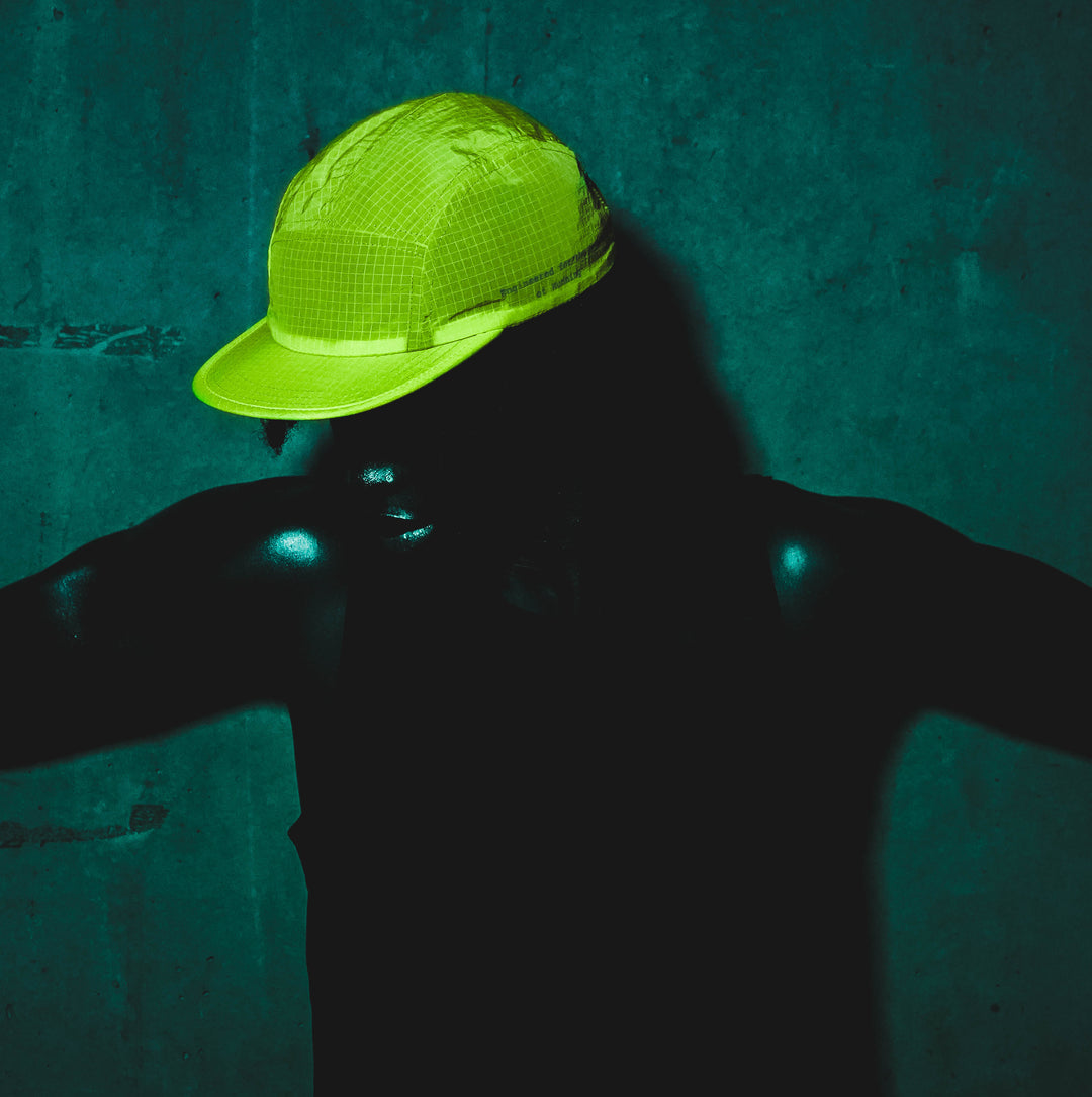 Side profile of a female runner wearing a white cap, pink sports sunglasses, and a zip-up performance top.