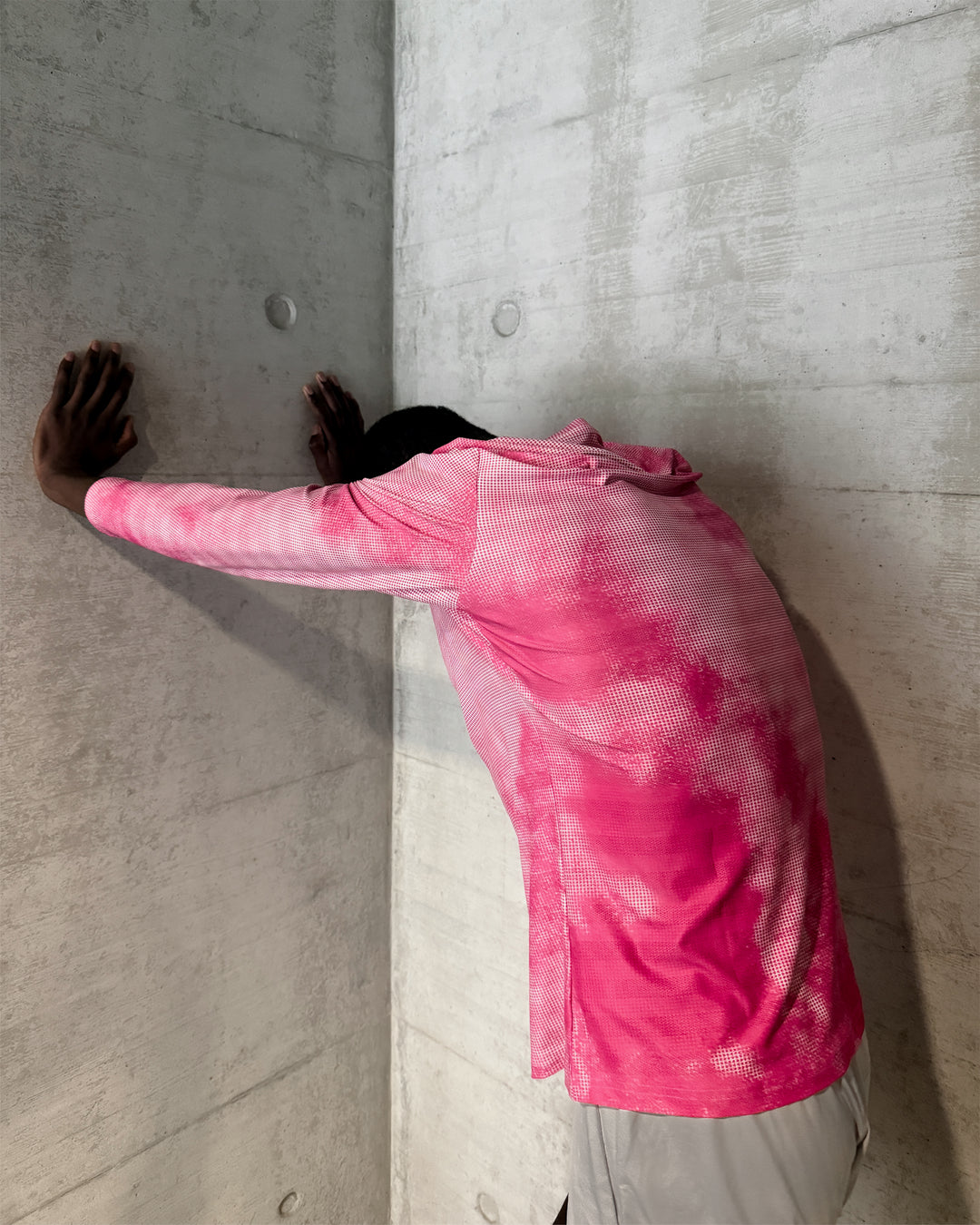Person wearing a pink lievre running long sleeve shirt against a concrete wall.