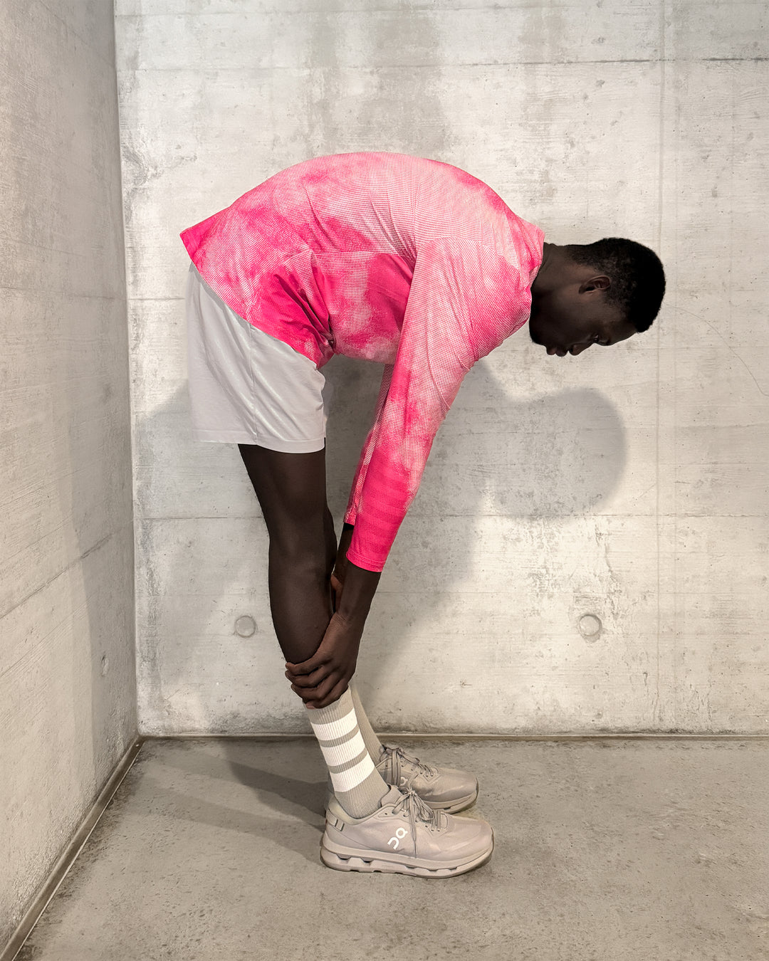 Person wearing a pink lievre running long sleeve shirt and gray shorts against a concrete wall.