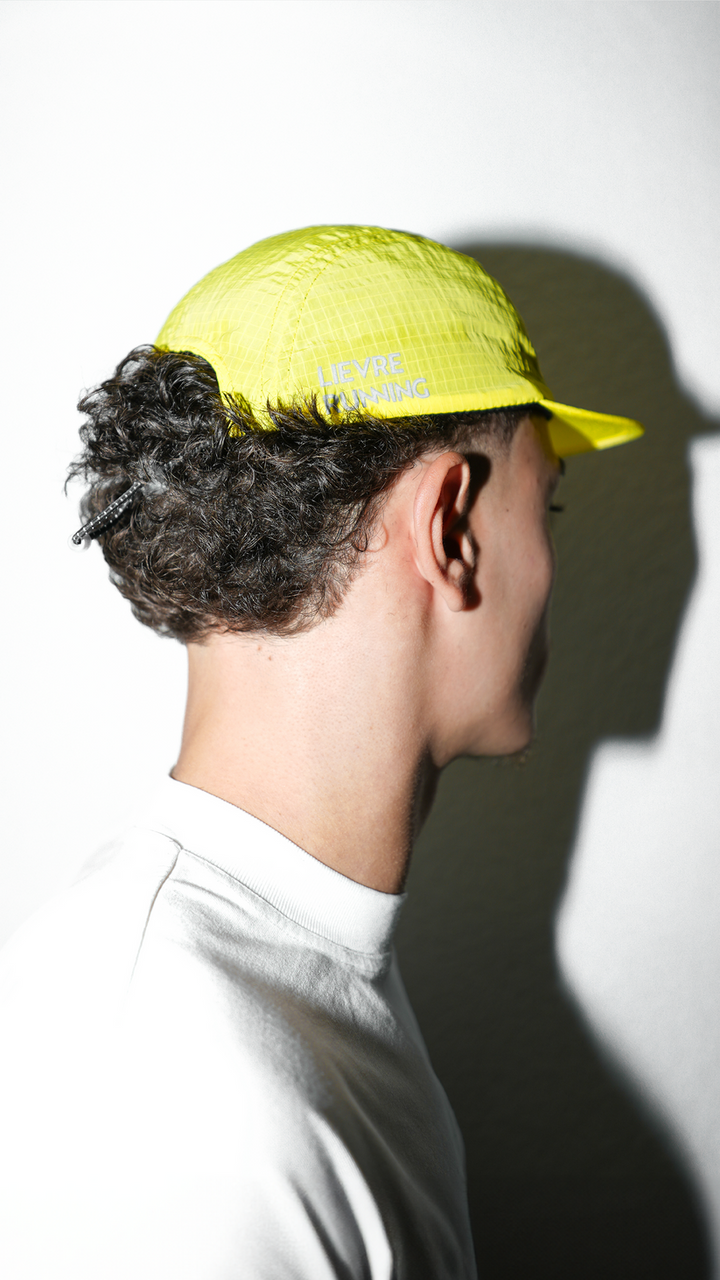 Lievre Running yellow performance running cap, lightweight technical fabric with adjustable back cord and “Engineered for the Art of Running” text on the side panel.