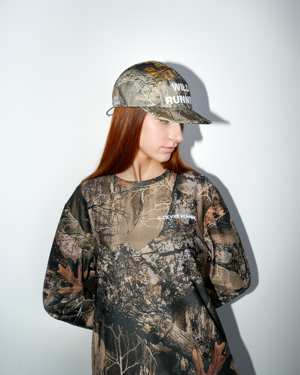 Lievre Running Wild Runner cap with camouflage print and bold “WILD-RUNNER” white text on front, five-panel silhouette with flat brim.