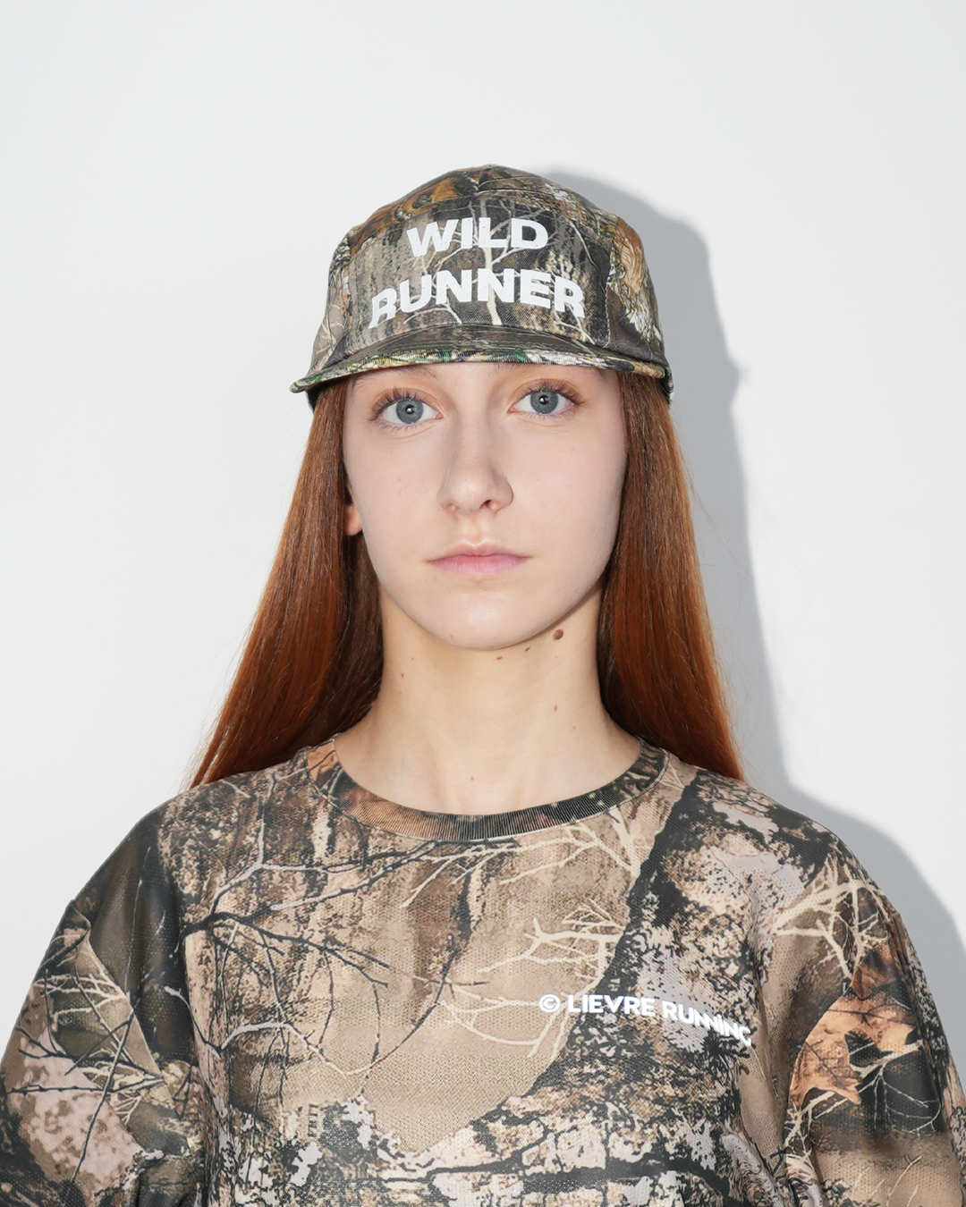 Lievre Running Wild Runner cap with camouflage print and bold “WILD-RUNNER” white text on front, five-panel silhouette with flat brim.