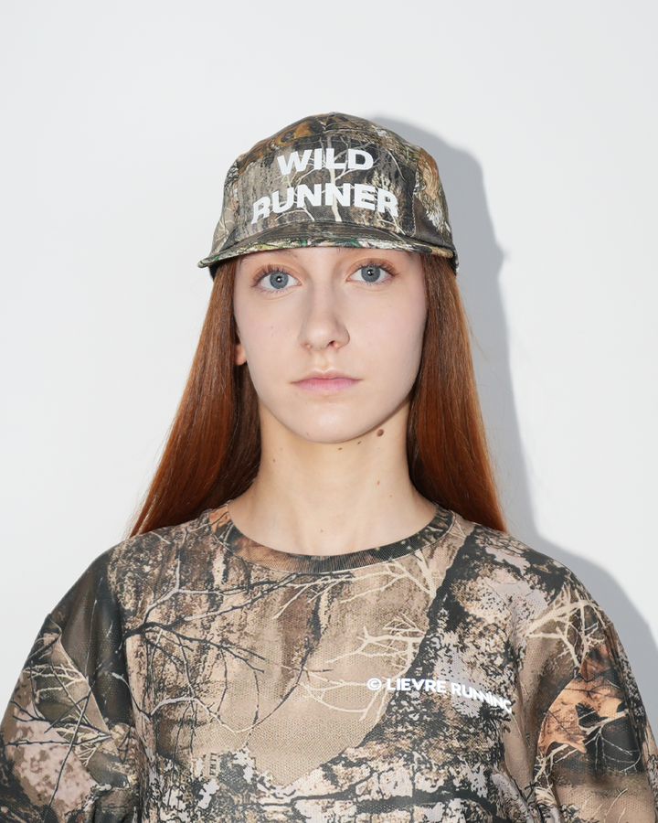 Lievre Running Wild Runner cap with camouflage print and bold “WILD-RUNNER” white text on front, five-panel silhouette with flat brim.