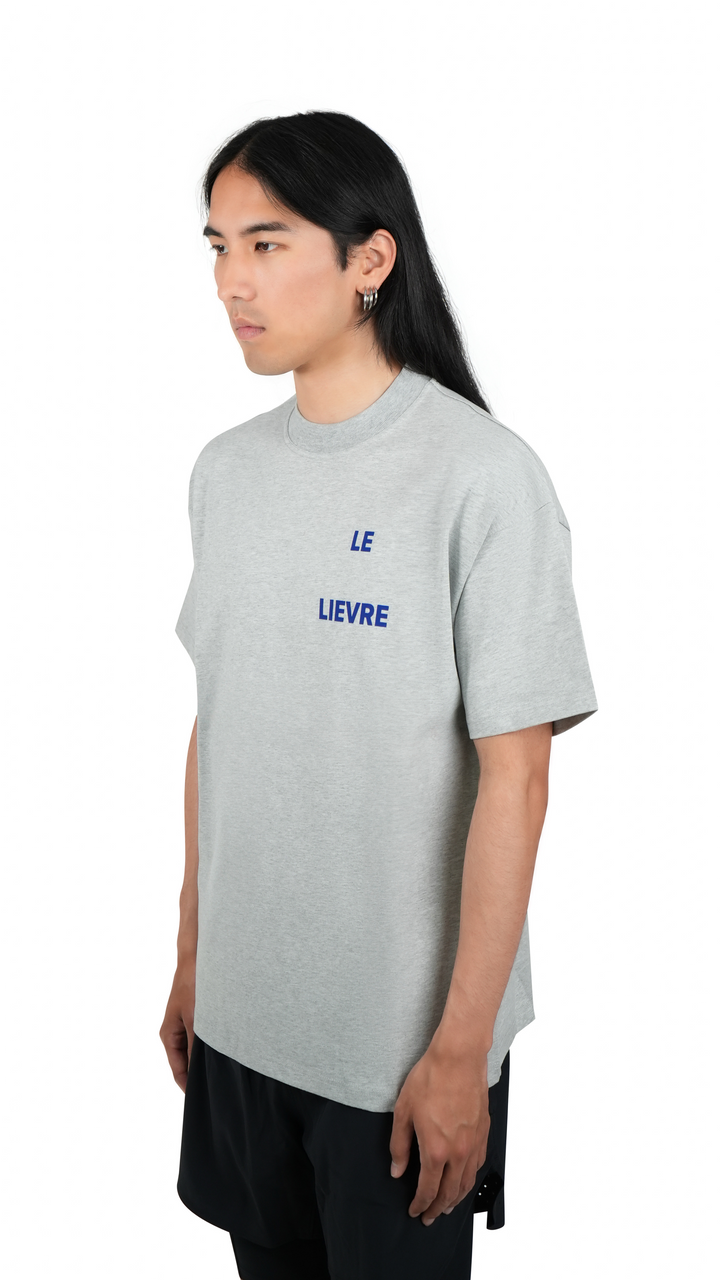 Lievre Running grey cotton tee with relaxed fit, featuring a large blue graphic of a running hare on the back and subtle script detail near the hem.