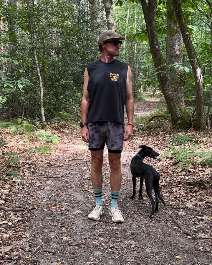 Man running on a trail in a forest wearing a black Nowhere Somewhere Running Peace tank top with yellow text.