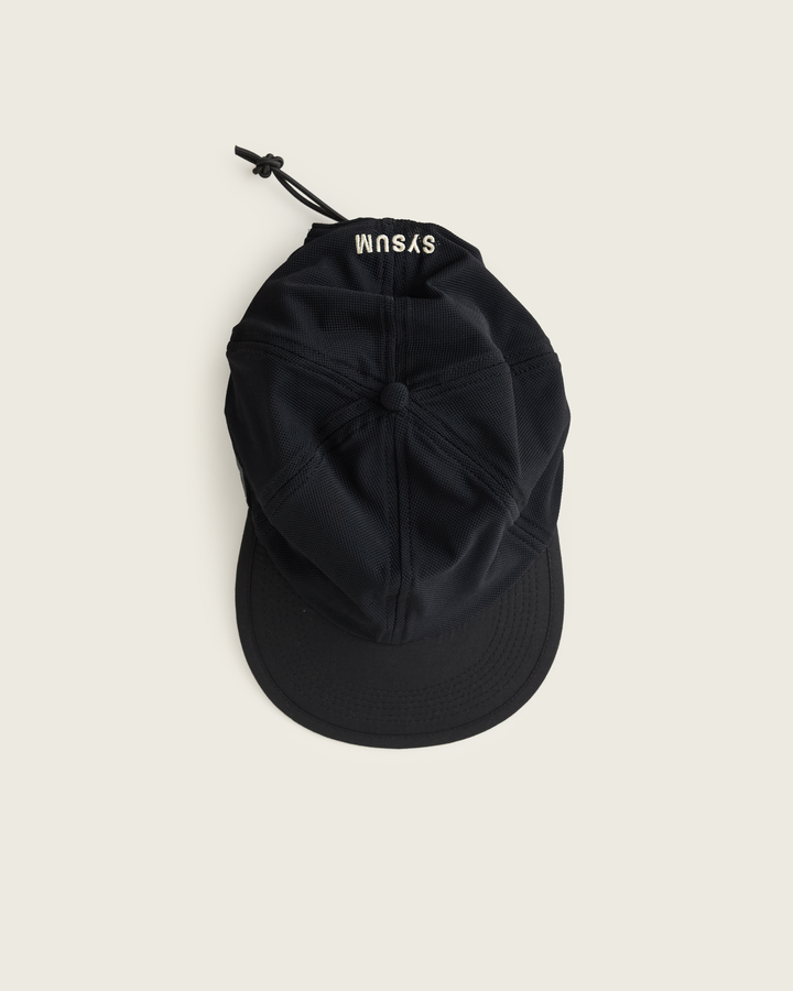 6-panel mesh running cap in Neutral and Black from Sysum, lightweight construction with soft foam bill and adjustable back strap visible, photographed in a neutral studio setting.