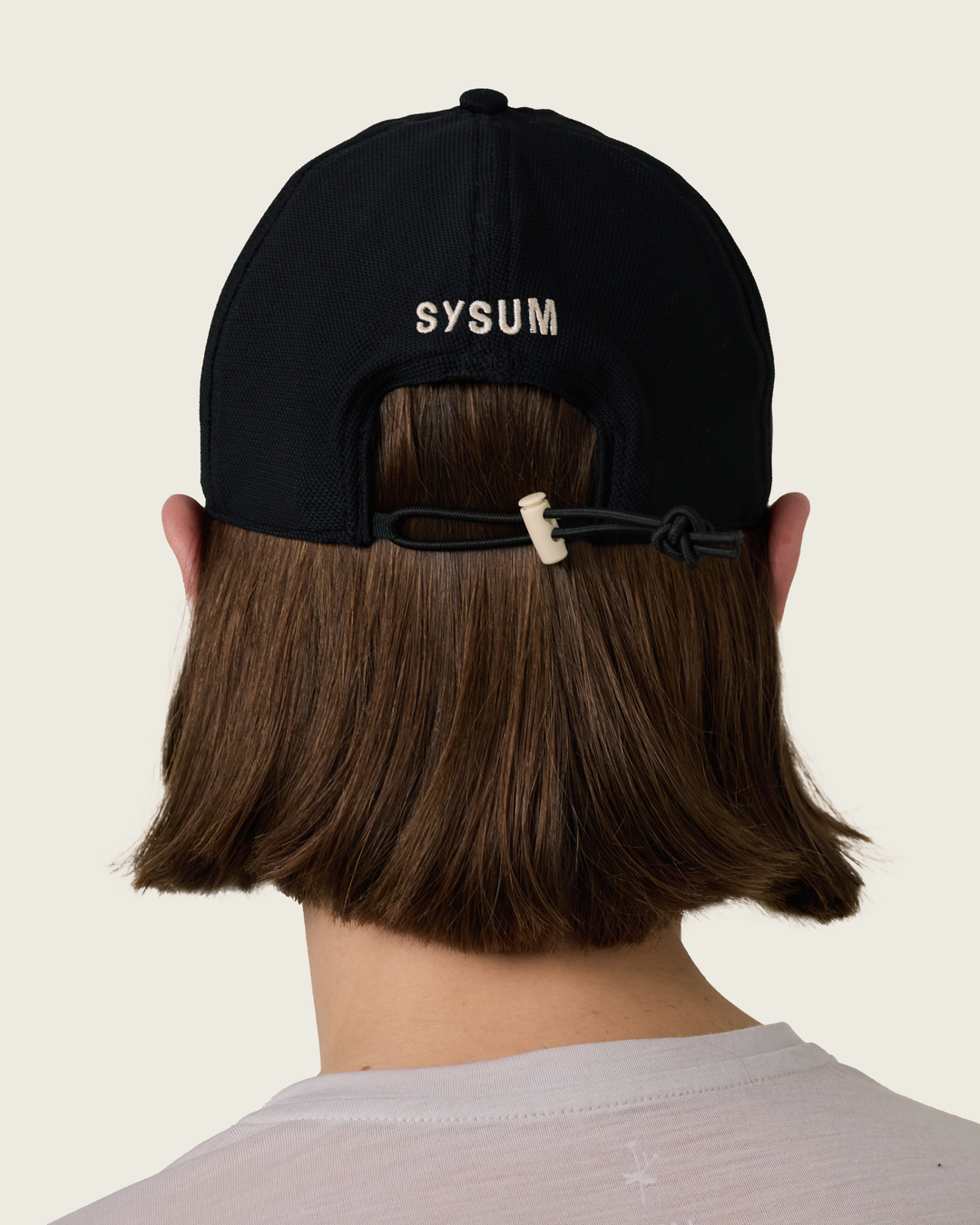 6-panel mesh running cap in Neutral and Black from Sysum, lightweight construction with soft foam bill and adjustable back strap visible, photographed in a neutral studio setting.