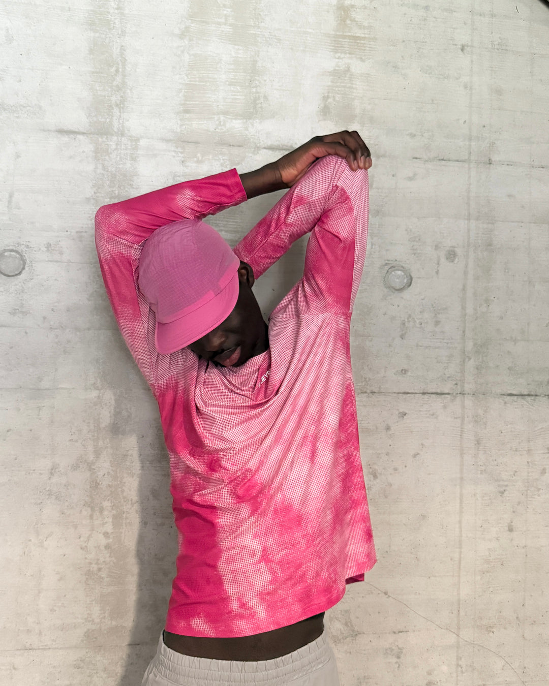 Person wearing a pink Lievre Runnin cap and matching shirt against a concrete wall
